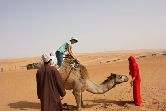 Getting on a camel at a Bedouin Camp in Oman riding a camel in Oman
