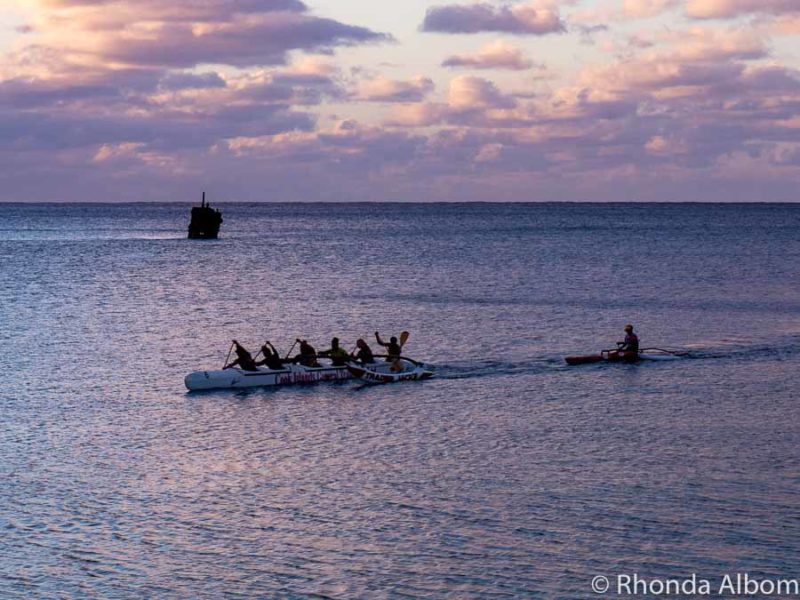 The wreck of the Matai sits in the background as an outrigger canoe sails by seen from Trader Jacks Restaurants, Rarotonga, Cook Islands