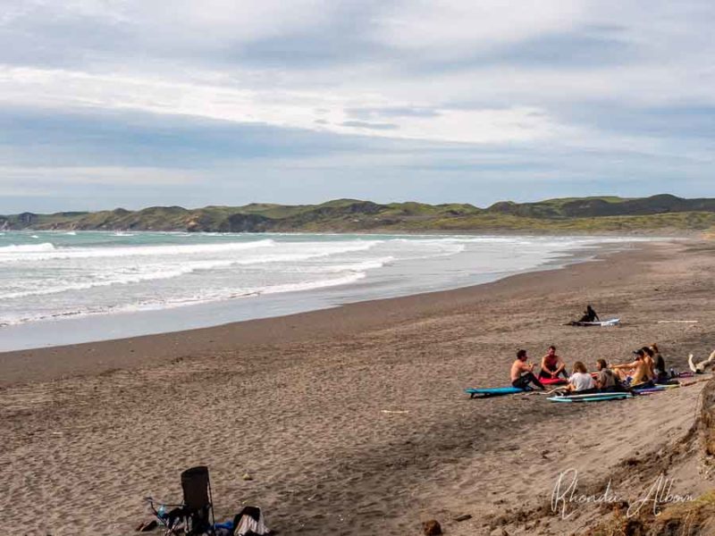17 Things to Do in Raglan: Unleash Your Adventurous Spirit 5 surfers resting on the sand at Ngarunui Beach in Raglan