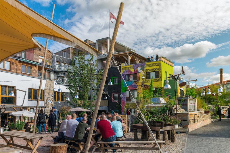 Colorful overview of a group of men sitting in wood benches at the Pampa beach bar and chilling while having a beer in the Holzmarkt, near the Spree river.