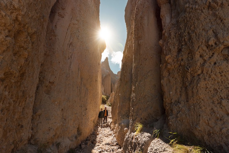 Two people walking in a narrow passage way at the Omarama Clay Cliffs