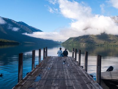 Couple sitting at the end of the pier at Nelson Lakes National Park is one of the most places to visit in New Zealand