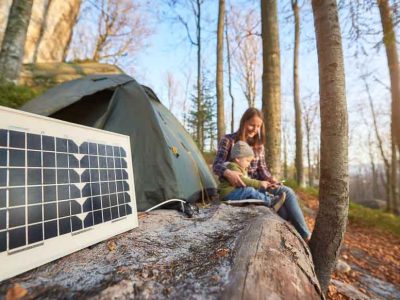 Portable solar generator for camping next to a tent on a sunny day with mom and small child using a phone