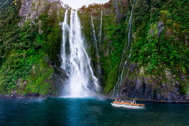 Stirling Falls at Milford Sound in South Island of New Zealand. Tourist ferry approaching Stirling Falls, the greatest waterfalls in Milford Sound, New Zealand.
