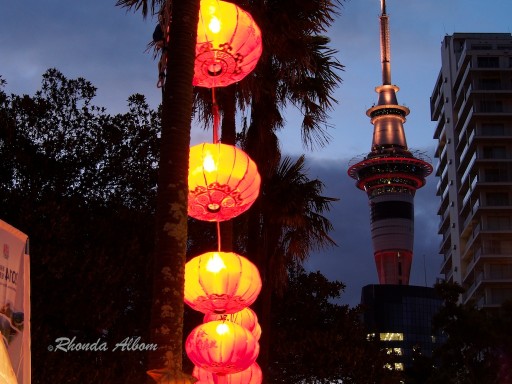 The Auckland Sky Tower light up at night with colourful Chinese lanterns in the foreground.